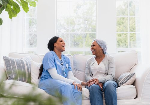 The mid adult female home healthcare nurse and the senior adult female cancer patient share a lighthearted moment together during a home visit.