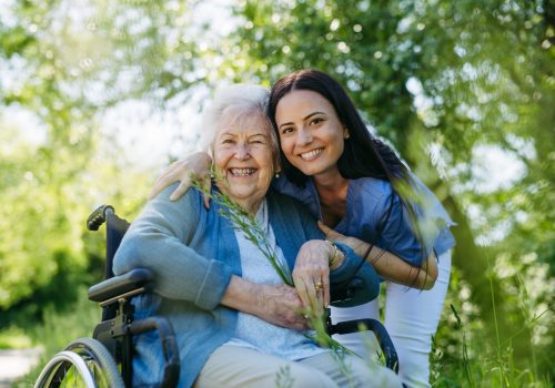 Female caregiver and senior woman in wheelchair. Nurse and elderly woman enjoying outdoor stroll during warm day in nature.